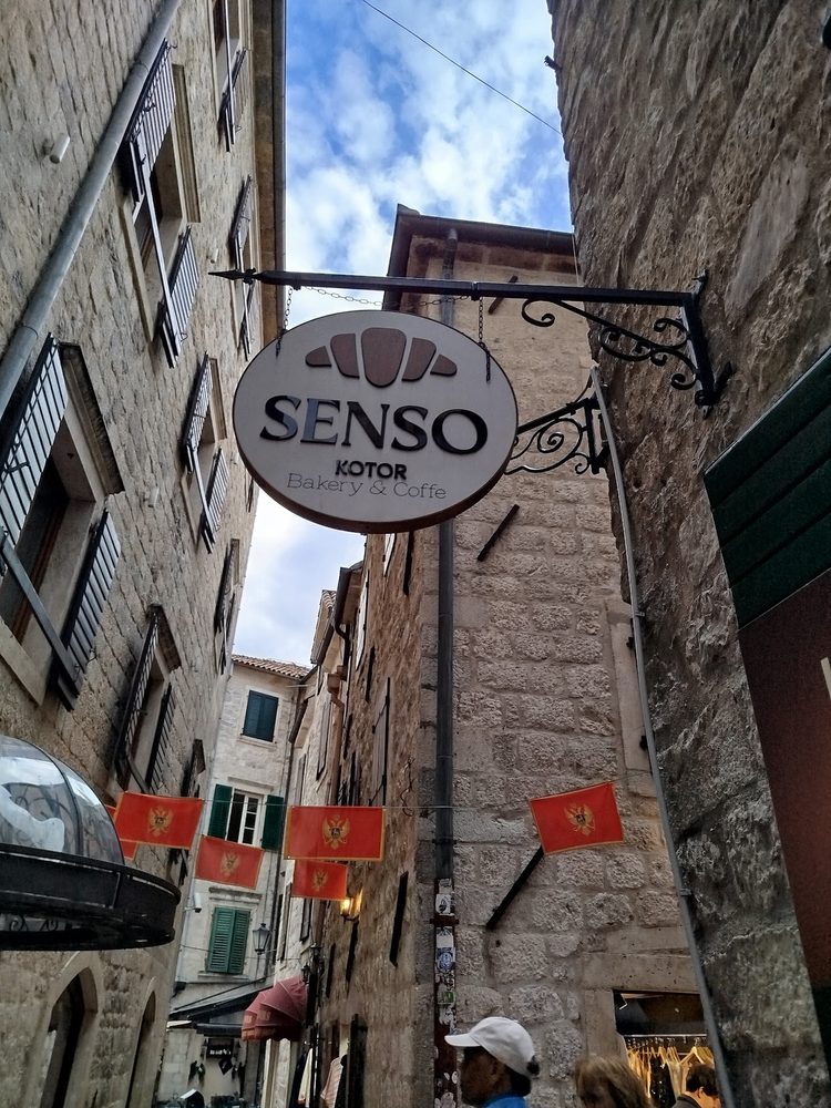 Tabla Senso Kotor Bakery & Coffee u uličici sa crnogorskim zastavama